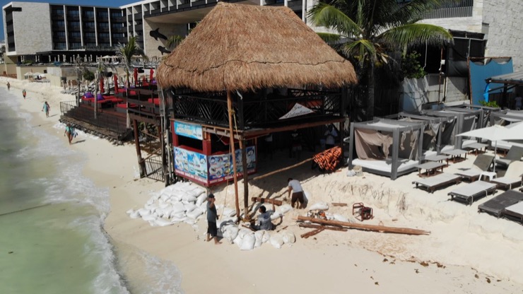 A building on stilts is using sand bags to keep the stilts up. The sea is very close by.